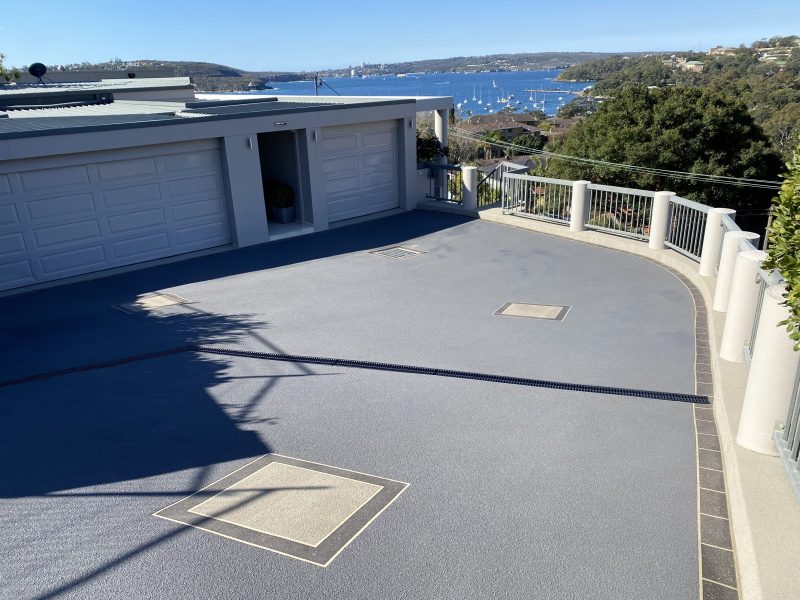 Resurfaced concrete driveway in Mosman on Sydney's Lower North Shore, finished in a textured non-slip grey with sandstone-bordered inset panels, overlooking Middle Harbour